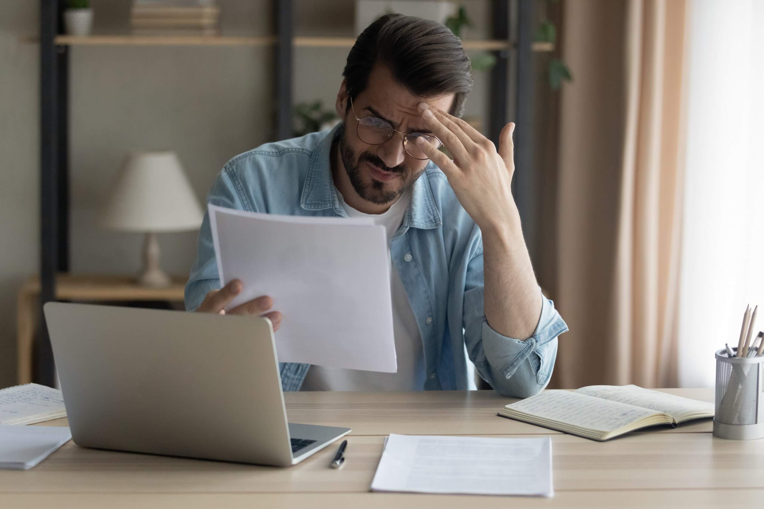 Confused young businessman holding paper letter informing about accumulated debt